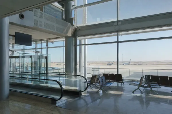 An empty modern airport transit concourse overlooking unbranded aircraft and an arid horizon