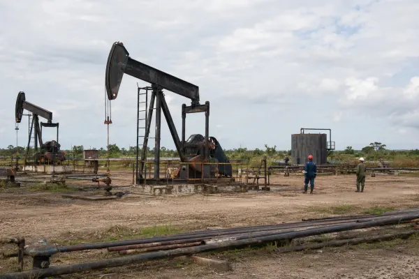 A weathered oil field with pumpjacks, pipes, storage equipment and two distant workers