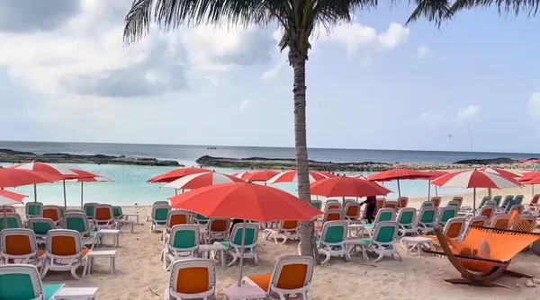 Guarda-sóis vermelhos e brancos protegem fileiras de espreguiçadeiras coloridas na areia da Hideaway Beach, com vista para as águas turquesas da ilha privada da Royal Caribbean, Perfect Day at CocoCay.
