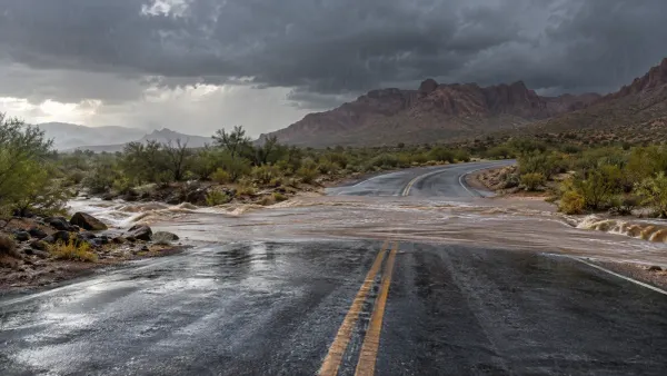 Monsoon rain sending muddy water across an empty desert highway beneath dark clouds in Arizona