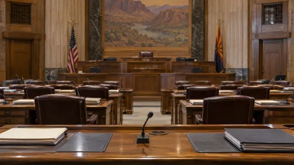 An empty, neutral legislative hearing room with wooden desks, microphones and document folders.