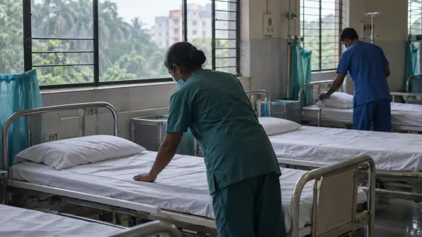 Un área de admisión de un hospital sin nombre en Bangladés durante la temporada de monzones, donde personal anónimo prepara camas vacías bajo la luz natural