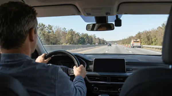 Driver on a divided highway with a generic aftermarket driver-assistance device mounted near the rearview mirror