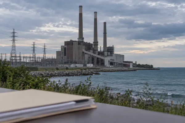 A large coal-fired power station and transmission lines beside Lake Michigan under an overcast sky, with an unmarked legal folder in the foreground.