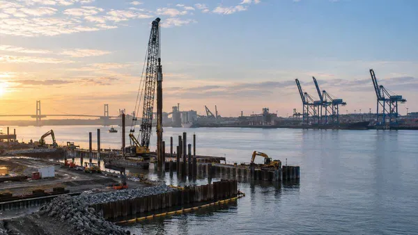 Marine construction equipment and container cranes beside a broad river at dawn