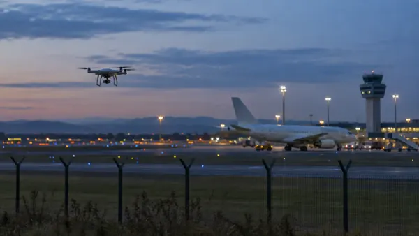 Un pequeño dron vuela cerca del perímetro de un aeropuerto genérico al anochecer, mientras un avión de pasajeros sin marca…
