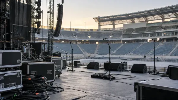 An empty unbranded stadium concert stage prepared with microphones, road cases and audio equipment at dawn.