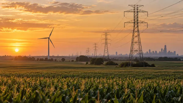 Power lines cross Illinois farmland with a wind turbine on the horizon.