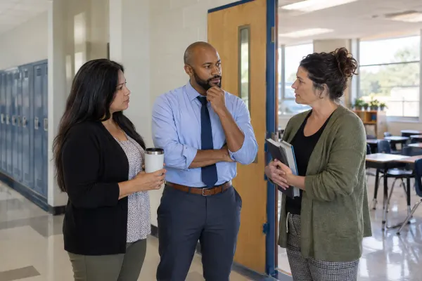 Three school staff members confer in a public school hallway before classes.