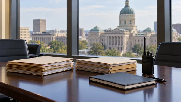 Illustrative state-government policy workspace with plain folders and the Indiana Statehouse softly blurred in the background.