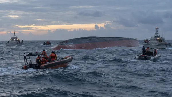 Indonesian search-and-rescue vessels surround an overturned passenger ferry in rough Java Sea waters at dawn.