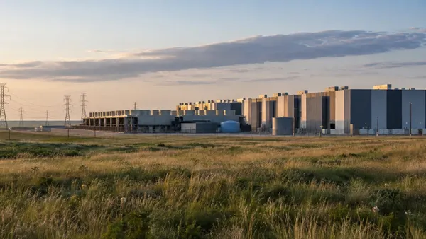 A large unbranded data center campus beside Kansas prairie grass and high-voltage transmission lines.