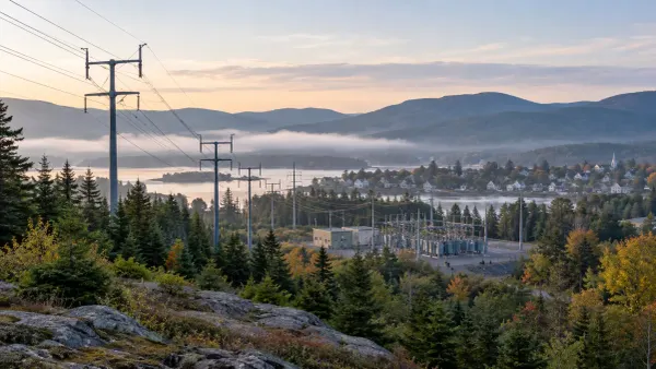 Power lines and a substation crossing a wooded Maine landscape at dawn