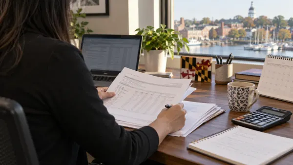 Payroll manager reviewing records at a desk overlooking a Maryland harbor