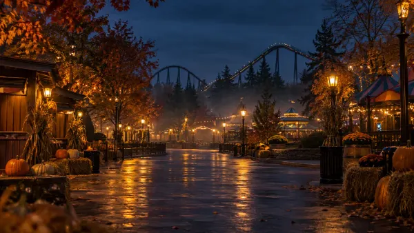 A generic amusement park midway decorated for autumn at night with a distant roller coaster