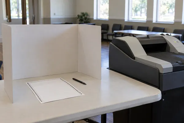 A generic absentee voting setup with a blank paper ballot, privacy folder and optical scanner in a quiet civic office