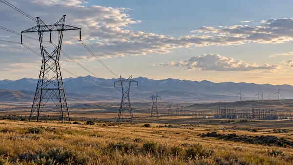 Transmission lines crossing a Montana landscape beneath a neutral evening sky