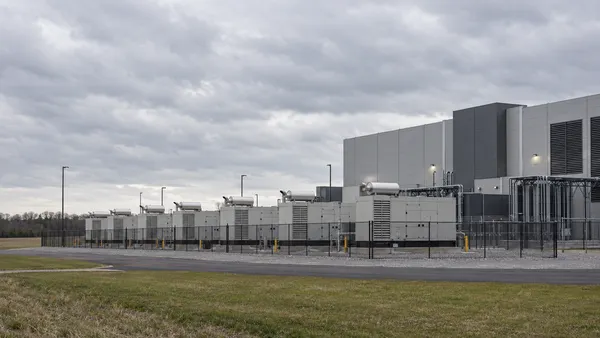 A generic modern data center with enclosed generator units behind a low fence under an overcast sky.