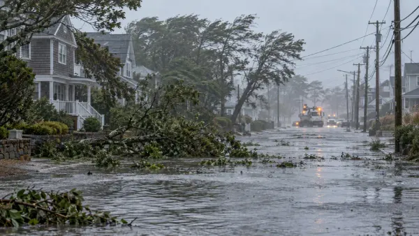Águas da inundação e ramos caídos cobrem uma rua residencial costeira enquanto as equipas de serviços públicos trabalham durante uma tempestade de inverno.