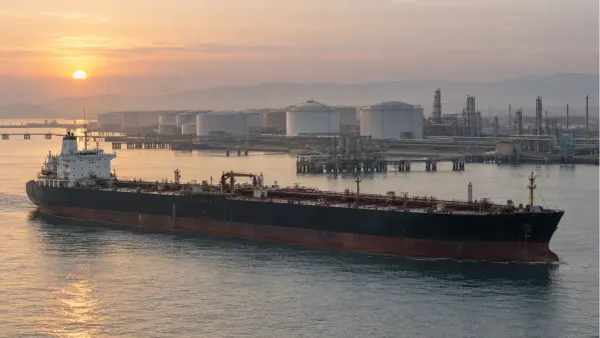 An unbranded crude-oil tanker passes a coastal energy terminal in early-morning light.