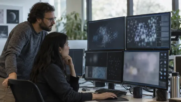 Two AI safety researchers review model activity on monitors in an unbranded operations room.