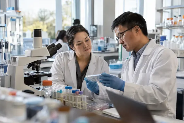 Two university biomedical researchers examine a sample tray together in a naturally lit laboratory.