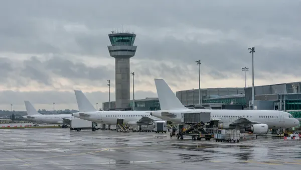 Unbranded passenger aircraft parked beside an airport control tower under overcast skies