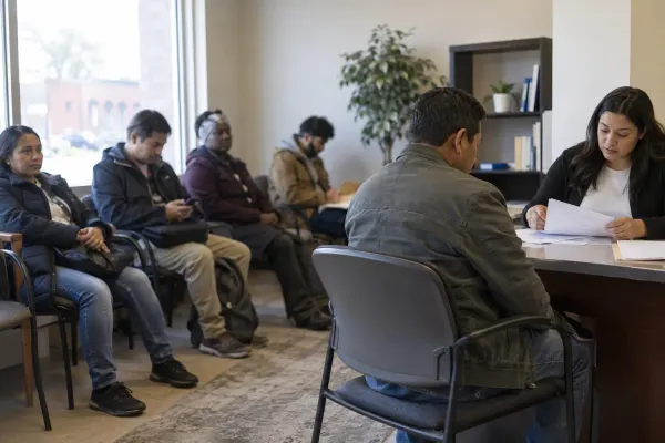 People wait while a client reviews paperwork with a caseworker in a legal-services office.