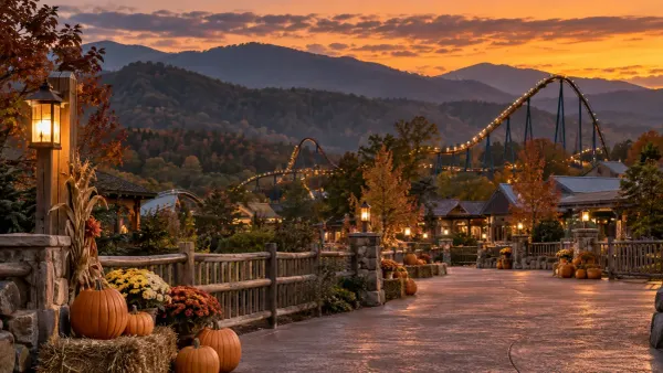 An autumn amusement park walkway with pumpkins and a lit roller coaster against Tennessee mountain ridges at sunset.