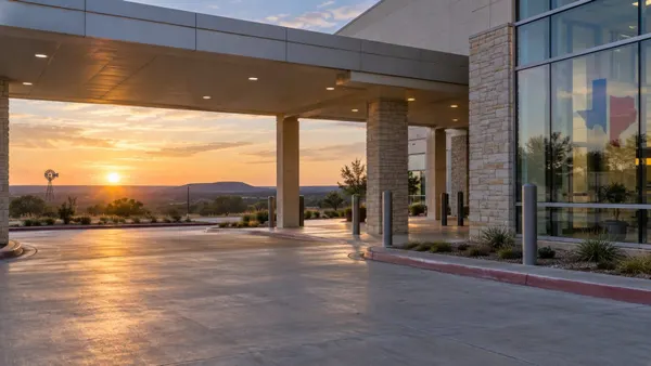 A quiet modern Texas hospital entrance at sunrise overlooking a rural landscape.