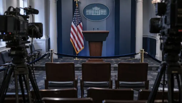 Three empty chairs behind a velvet barrier in a symbolic White House press briefing room