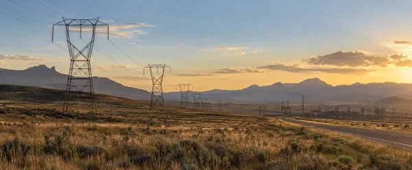 Illustration of high-voltage transmission lines crossing Wyoming rangeland near a distant substation at sunset.