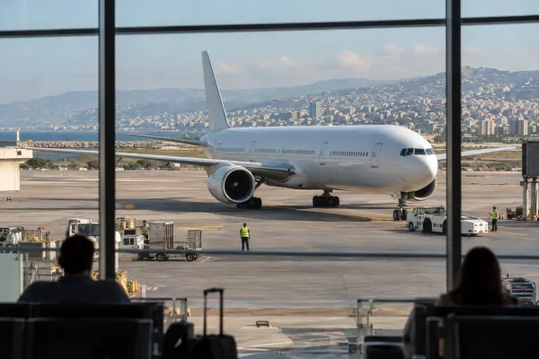An unbranded wide-body passenger aircraft taxis at Beirut’s international airport as travelers watch through a terminal window.