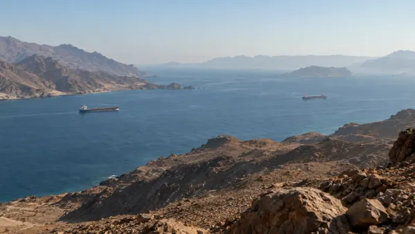 Navios de carga atravessam um estreito canal do Mar Vermelho, ladeado por montanhas áridas e acidentadas.