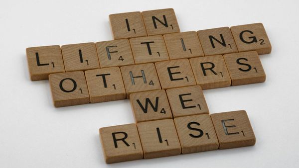 Scrabble letters arranged to spell "In lifting others we rise."