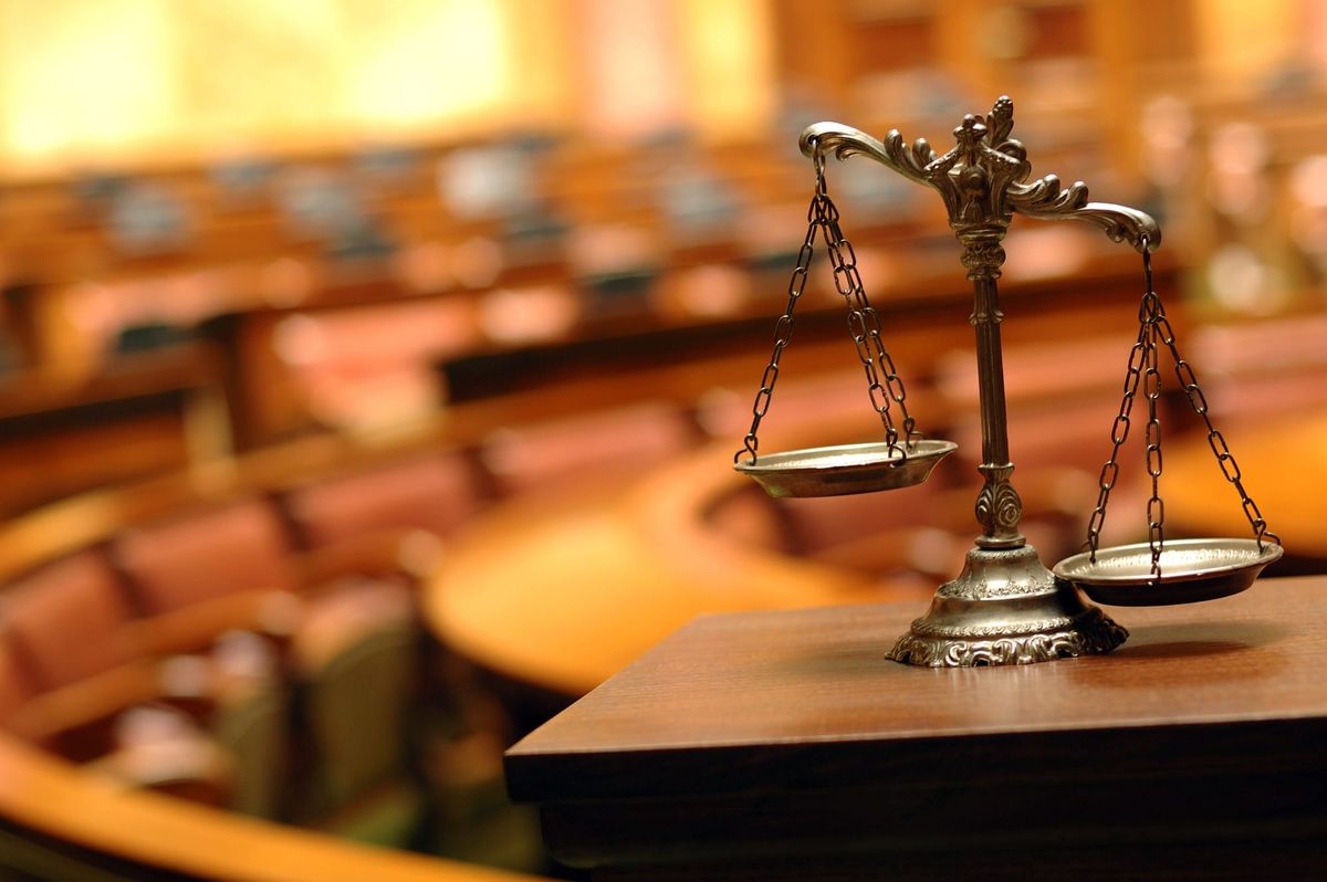 A close-up of a brass scale of justice on a wooden surface in a courtroom setting. 