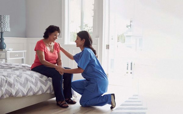 A nurse kneels in front of a patient to console her.