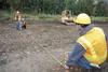 Alaska Job Corps Center student Levi Brence holds the end of a tape measure as Eric Joe and Harry Albert get ready to take a reading and mark a spot in the dirt for a new recycling center dro