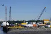 Cargo containers and construction materials are stacked below cranes at the Port of Alaska in Anchorage on June 12, 2025, as a plane flies overhead. The transportation and warehousing sector 