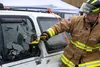 Nicholas Parks, a 673d Civil Engineer Squadron firefighter, uses a multitool to break the window of a damaged car for a vehicle-extrication demonstration during Fire Prevention Day at Joint B