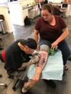 Tattoo artist Gabe Brause works to remove unwanted lettering from Sydney Hinkley’s leg. AMY ARMSTRONG/For The Eagle