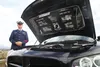 Alaska State Trooper Chris Green stands in his Coast Guardsman’s uniform next to the open hood of his souped up, customized Dodge Charger R/T. Green has two cars that match his two careers. H
