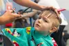 Gideon Warriner, 4,of Wasilla, is not too wild about getting his bangs cut at the Menard Center Tuesday afternoon by stylist Lacey Redick from Style Starts Here Hair Academy as part of Mat Su