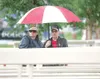 ROBERT DeBERRY/Frontiersman Renee and Glen Clifford sit under an
umbrella and wait for the start of the Kenai Senior Center’s
Toe-Tappin’ Country performance at the Colony Stage Thursday on t