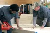 Chris Haugom holds a board steady as Travis Friesen prepares to nail two together at a cabin building workshop at Friesen's Custom Cabins off Soapstone Road in Palmer on Saturday. Though the 