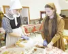 ROBERT DeBERRY/Frontiersman Dressed as a Pilgrim and an Indian,
Hosanna Hale, 17, left, and Heather Shields, 16, place sweet treats
on a platter in preparation for a fellowship Thanksgiving p