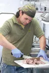 GREG JOHNSON/Frontiersman Shannon Million chops up a slab of
smoked pork at the Snow Dawgs BBQ wagon along the Parks Highway in
Wasilla. The mobile kitchen is finding a following for its Sout