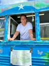Parbati Karki greets a customer from her distinctive blue bus. The Karki Food Bus recently celebrated one year of service from its roadside location in the parking lot of the Houston Grass St