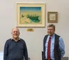 Mat-Su College Library Director Craig Ballain [left] and Campus Director Talis Colberg [right] stand in front of a Fred Machetanz painting donated by Sallie and Phillip Hamm.