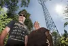 Doug and Brenda Lampton stand on the edge of their property with a cellular tower dominating the background. The two were surprised to learn the tower had been erected on a neighboring proper